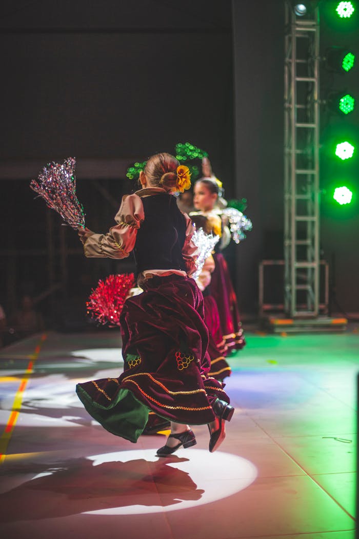 Women performing traditional dance on stage with colorful costumes and dynamic lighting.